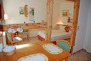 Une pièce chaleureuse avec une table en bois, deux chaises, un lit et une petite table de chevet avec une lampe.