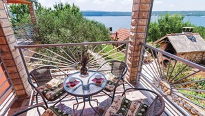 Un balcon avec une table ronde et des chaises en osier, donnant sur une étendue d’eau et une végétation luxuriante.