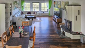 Een ruime woonkamer met een eethoek, een open haard en een groot raam met gordijnen.