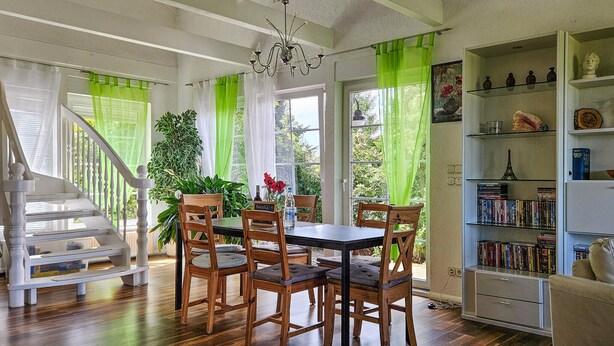 Een eetgedeelte met een houten tafel en stoelen, een kroonluchter en een boekenplank vol boeken en decoratieve objecten.