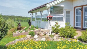 Een huis met een overdekte veranda, een windmolen en een tuin met gele bloemen.