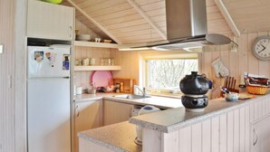 Cocina compacta con refrigerador, lavamanos y estufa. Hay una ventana que proporciona luz natural y un reloj en la pared.