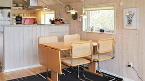 Un interior de madera con una mesa de comedor y sillas, una zona de cocina con estufa, y un ventanal con vistas a árboles.