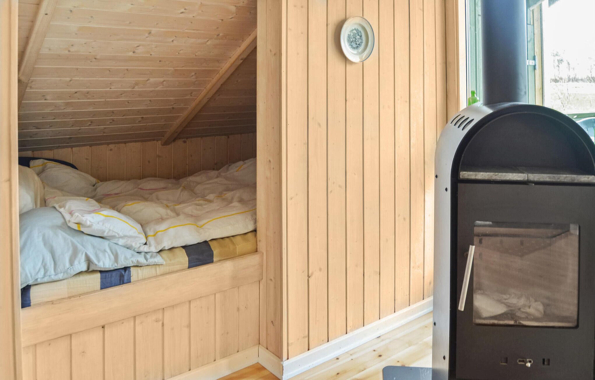 A cozy cabin with a wooden interior, a bed with a striped blanket, and a wood-burning stove.