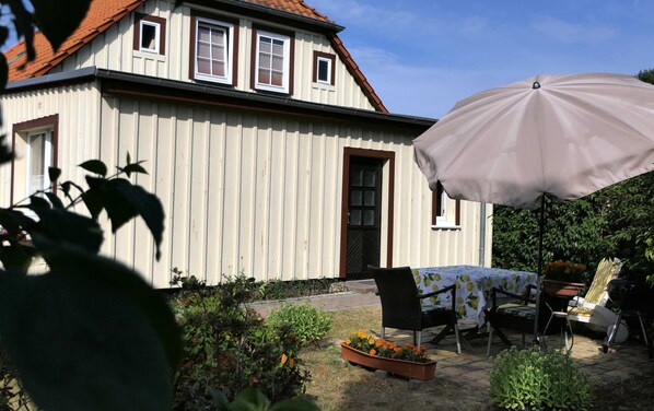 A white house with a red roof, a covered patio with a table and chairs, and a large umbrella.