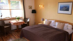 Een hotelkamer met een groot bed, een klein tafeltje met een vaas, een stoel en een lamp.