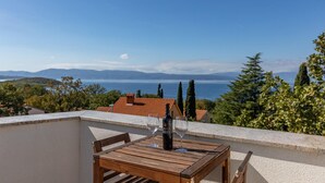 A wooden table with two wine glasses and a bottle on a balcony overlooking a scenic view of a lake and mountains. - Beach front apartment in Njivice with WiFi (Njivice)