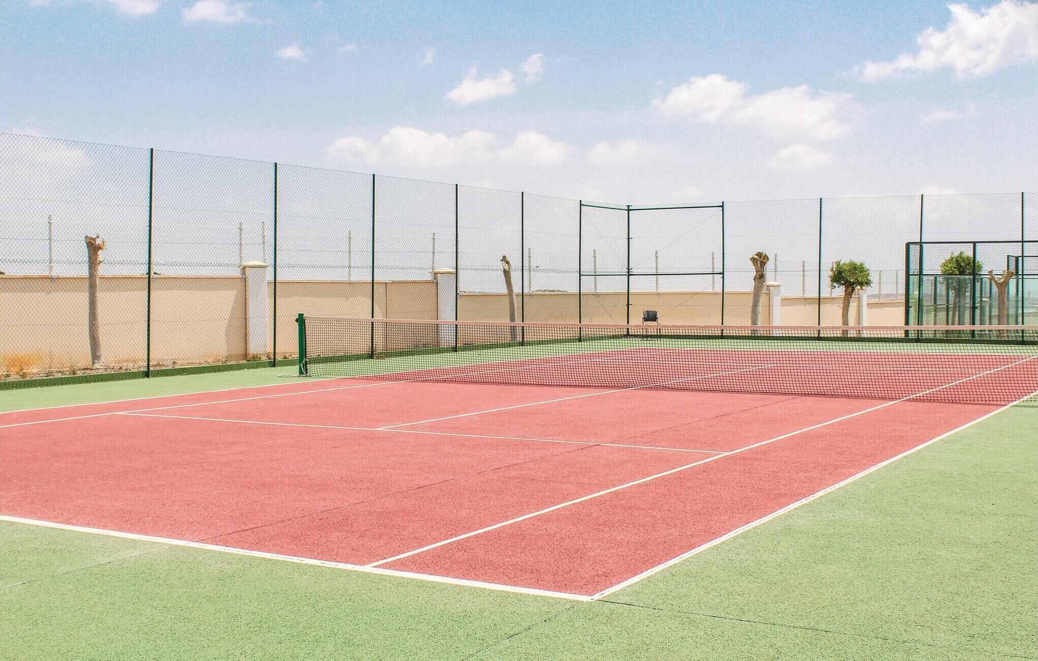 Een tennisbaan met een net, omringd door een hek, en een heldere lucht.