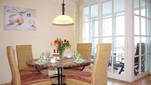 A dining area with wicker chairs, a round table, and a large window with a view. - (55) 3-room apartment with east-facing balcony - Appartementhaus Atlantik (Kühlungsborn)