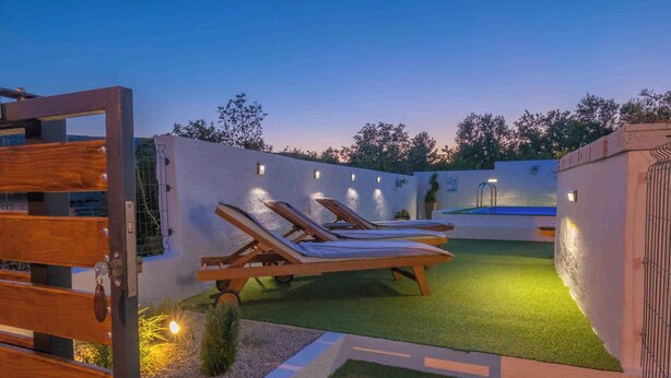 Ein Poolbereich auf dem Dach mit zwei Liegestühlen und einem kleinen Pool, umgeben von einer niedrigen Mauer und einer Holzpergola.