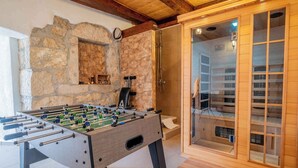 Ein Zimmer mit einem Kicker, einer Steinwand und einer Sauna.