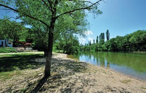 A riverside view with a building on the left, a tree in the foreground, and a clear sky.