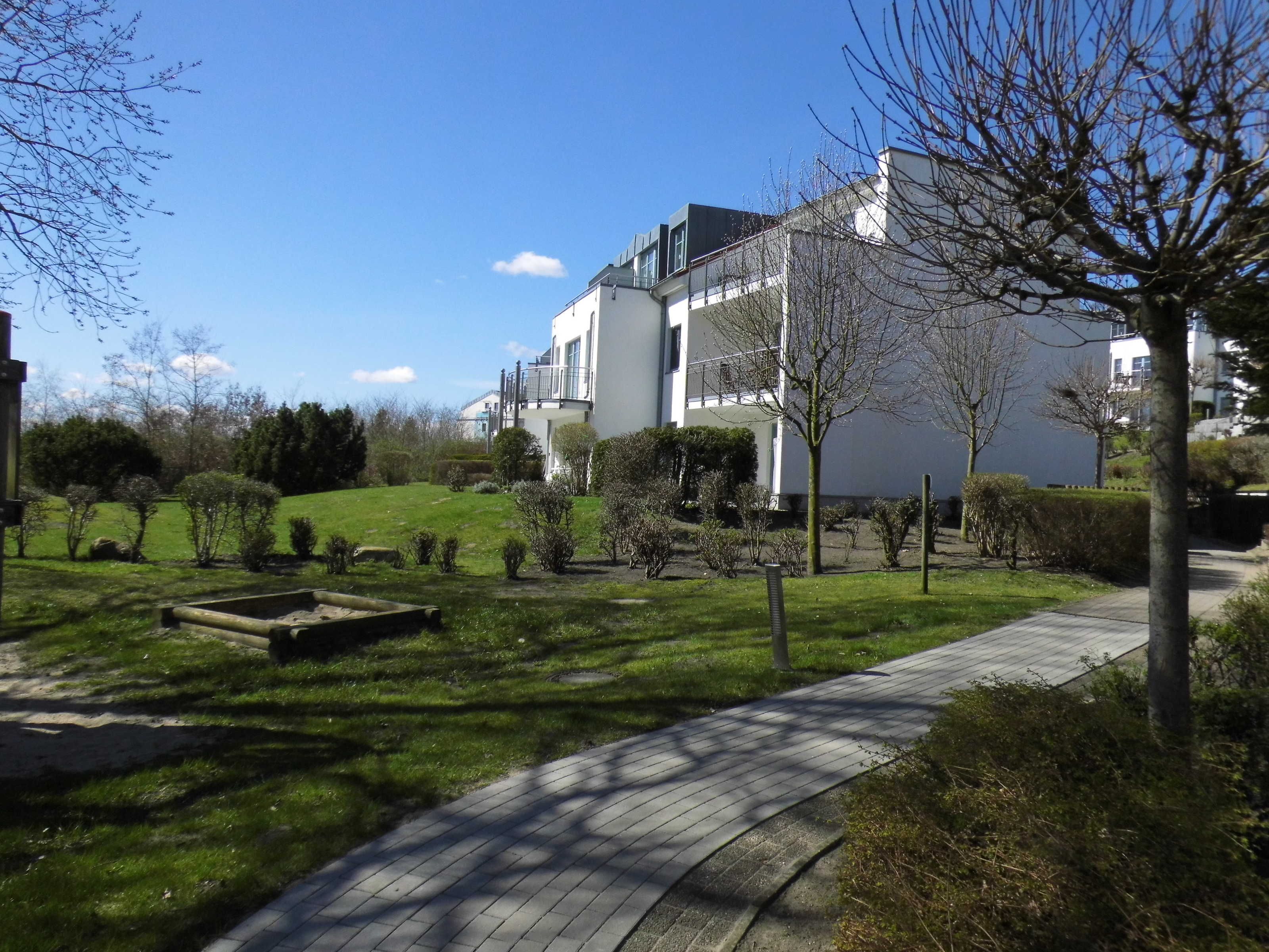 A residential area with a paved walkway, a grassy lawn, and a white building with a balcony.