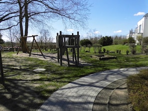 Ein Park mit einem Spielplatz, einem gepflasterten Weg und einem Gebäude im Hintergrund.