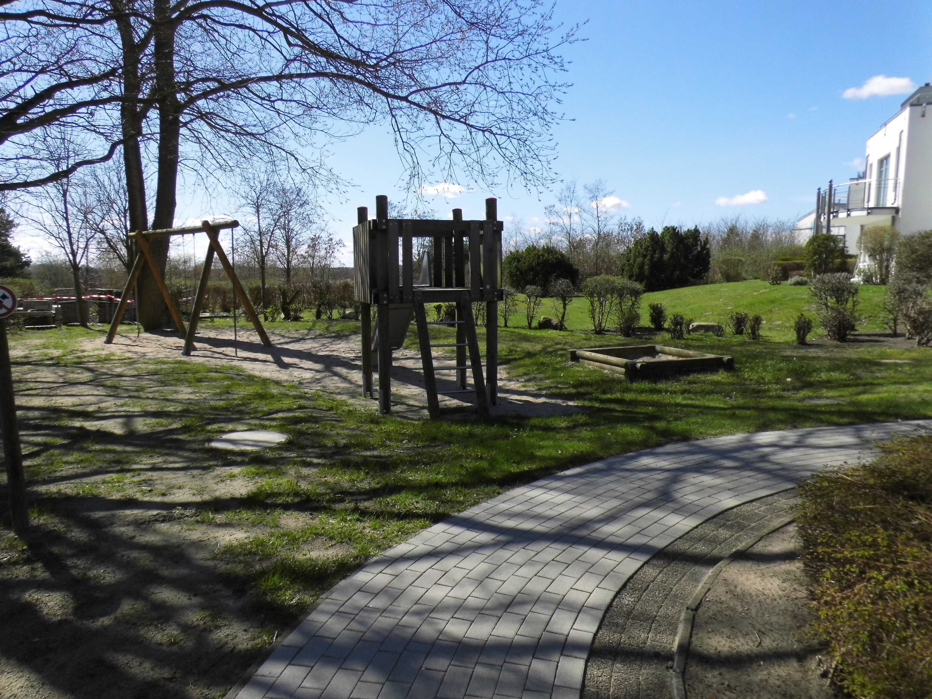 Ein Park mit einem Spielplatz, einem gepflasterten Weg und einem Gebäude im Hintergrund.