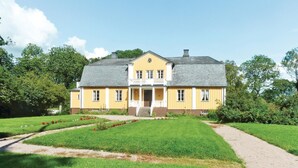 A two-story yellow house with a balcony, surrounded by a well-maintained lawn and trees. - Lovely home in älmhult with kitchen (Älmhult)
