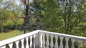A white balcony railing overlooking a garden with various trees and a red building in the background. - Lovely home in älmhult with kitchen (Älmhult)