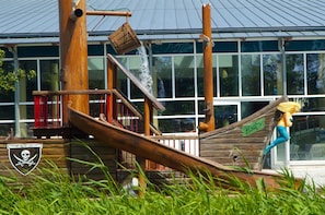 Ein Spielbereich im Piratenschiff-Design aus Holz mit Rutschen und einem Wasserspielzeug.