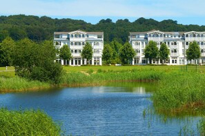 Ein großes, mehrstöckiges Hotel mit symmetrischer Fassade, gelegen am Ufer eines stillen Sees mit üppiger Vegetation und Bäumen.