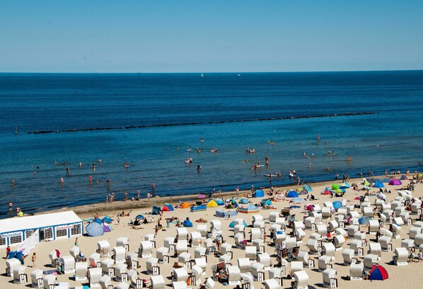 Ein Strand mit vielen Liegestühlen und Sonnenschirmen, einer Seebrücke, die ins Meer führt, und einem strahlend blauen Himmel.