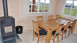 A wooden interior with a table and chairs, a black stove, and a window with a view of a house and grass. - Lovely home in Sydals with sauna (Sydals)