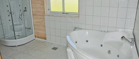 Ein Badezimmer mit einer gläsernen Duschkabine, einer Badewanne und einem Fenster mit Milchglas.