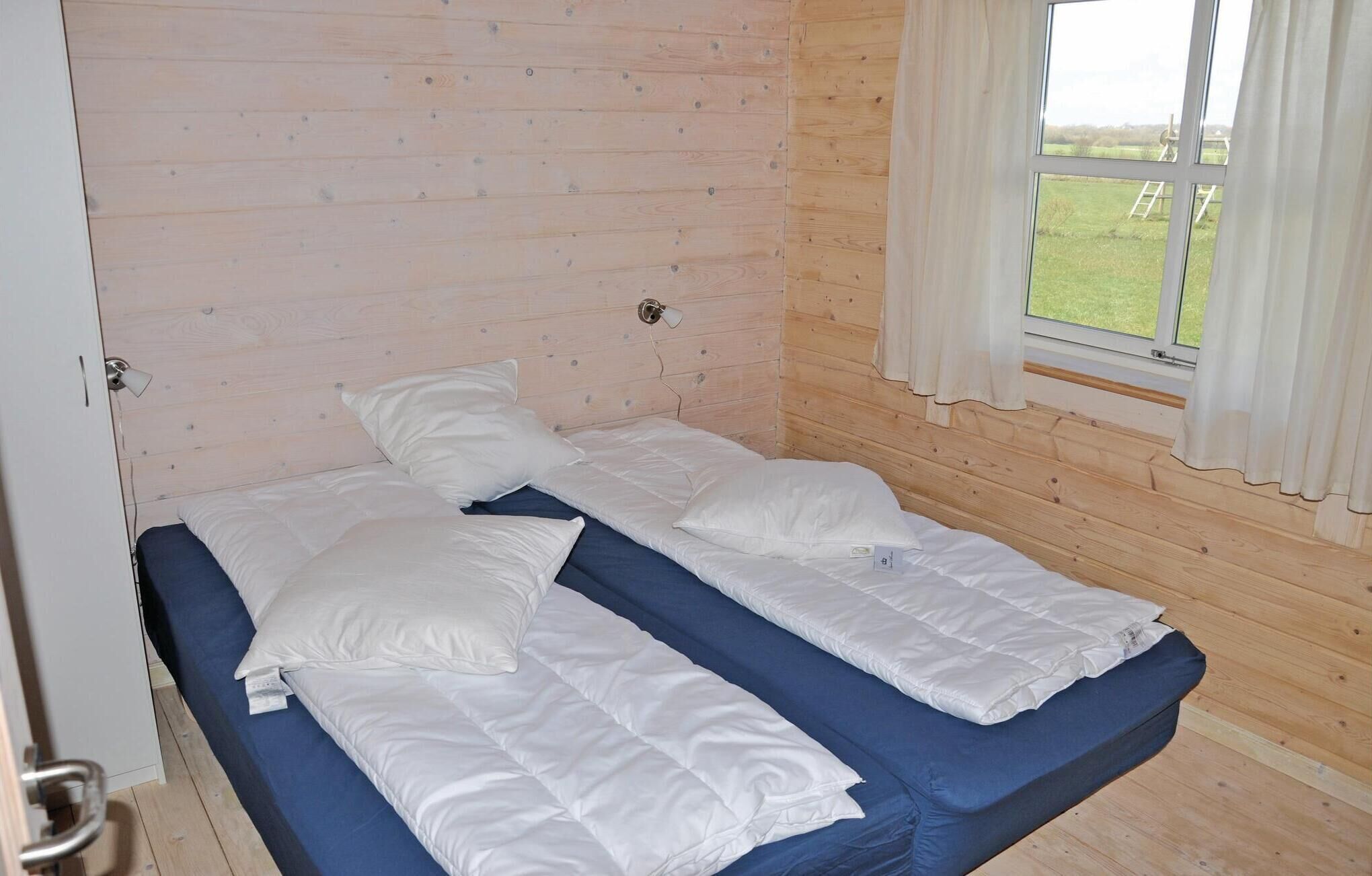 A single bed with white bedding in a room with wooden walls and a window with curtains.