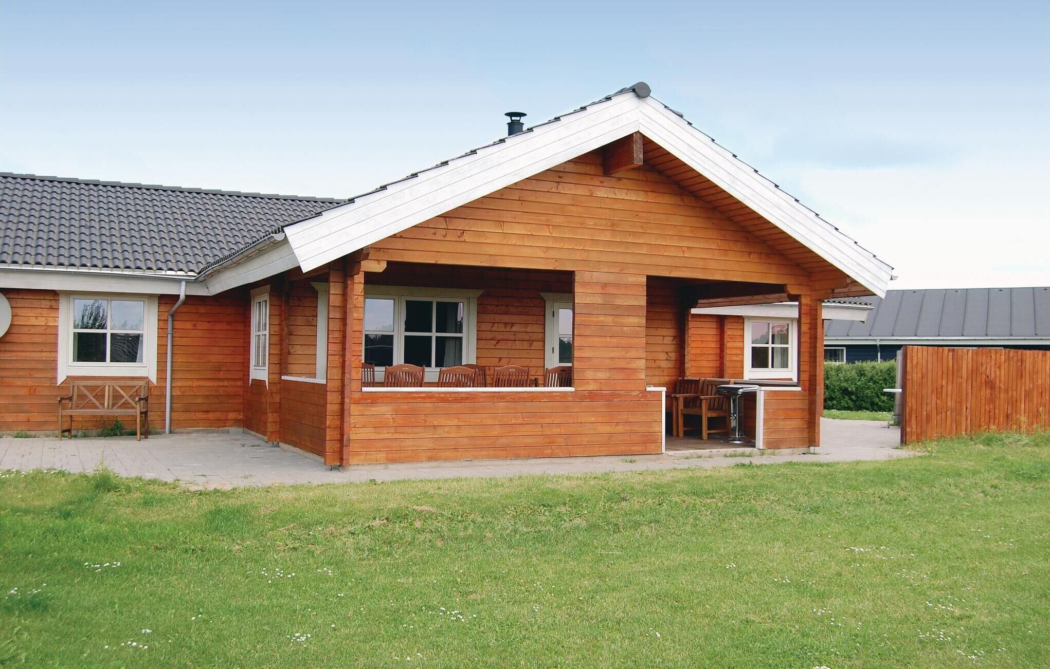 A wooden cabin with a sloped roof, a porch with chairs, and a small table.