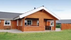 A wooden cabin with a sloped roof, a porch with chairs, and a small table. - Lovely home in Sydals with sauna (Sydals)