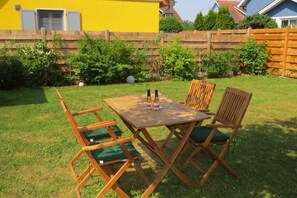 Une table en bois, quatre chaises, deux bouteilles de vin et deux verres, le tout posé sur une pelouse verdoyante.
