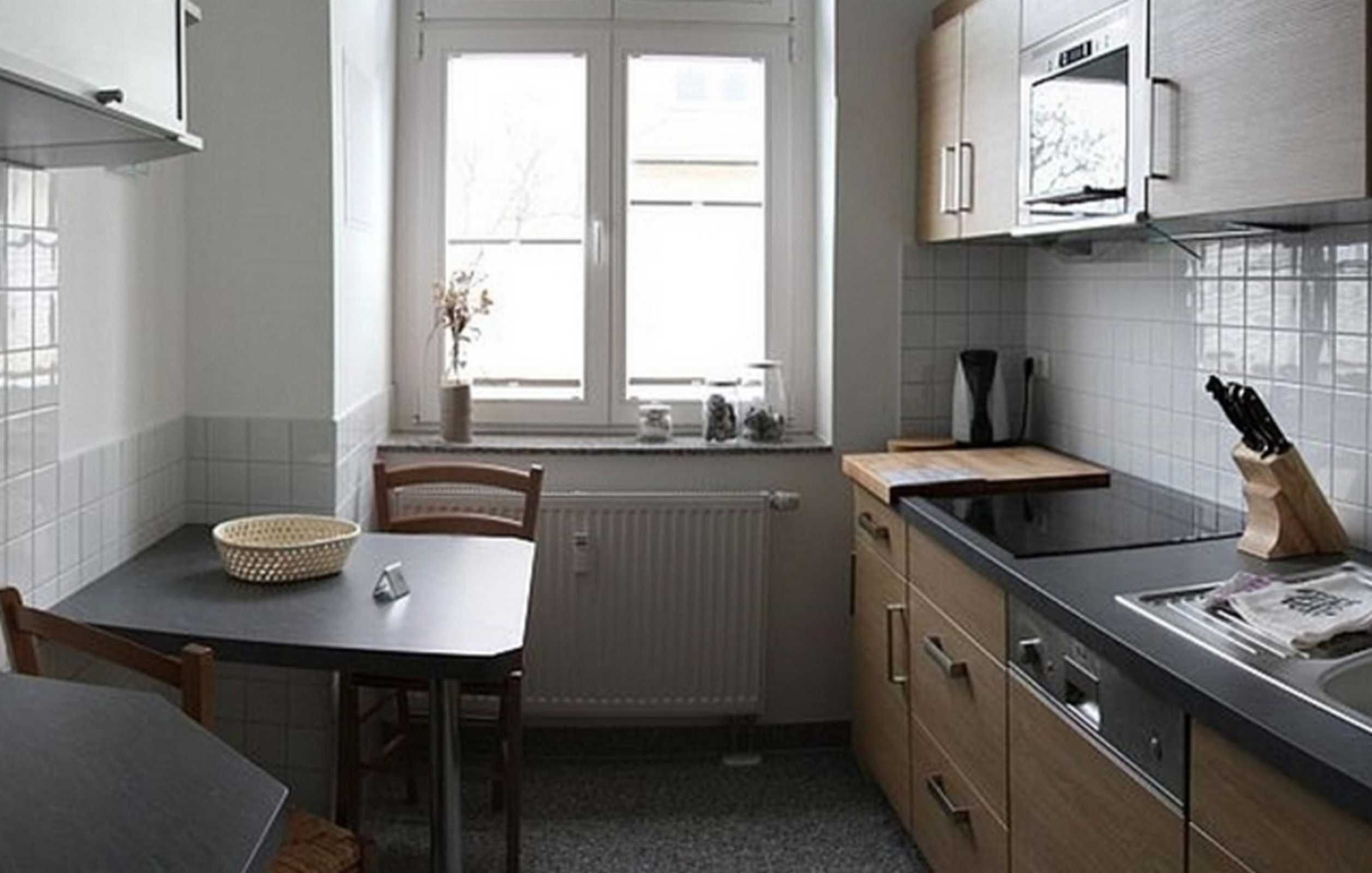 A compact kitchen with a window, white cabinets, a black countertop, and a wooden chair.