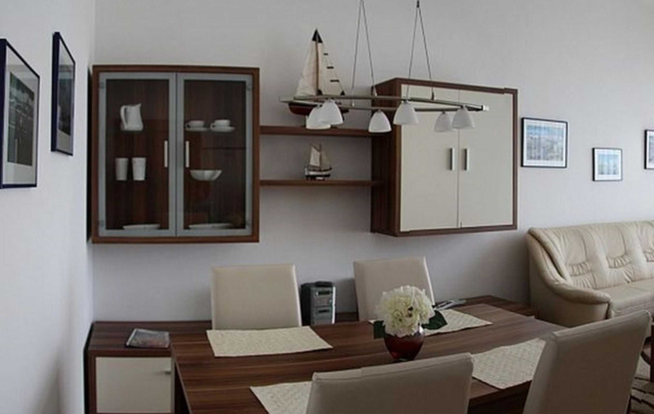 A dining area with a wooden table, white chairs, a cabinet with glass doors, and a sofa.