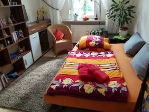 Un dormitorio con cama, una silla, una estantería y una ventana con plantas.