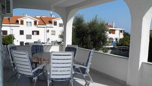 A covered outdoor patio with a table and chairs, overlooking a residential area with white buildings and red roofs. - Holiday apartment with air conditioning (Baška)