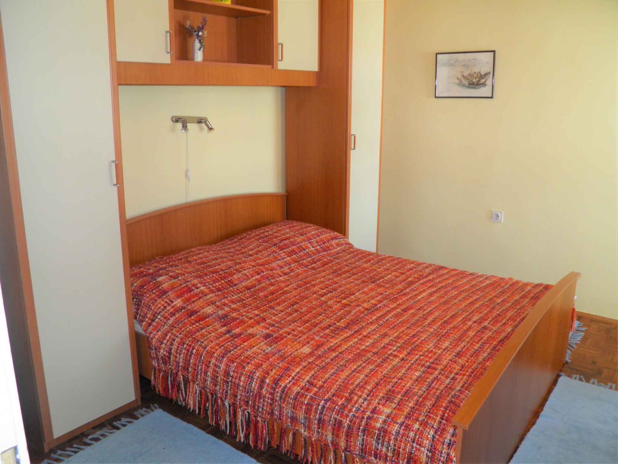 Une petite chambre avec un lit simple, une tête de lit en bois, une étagère intégrée au-dessus du lit et un tableau encadré au mur.