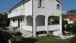 A white two-story building with a satellite dish, a balcony, and a small garden area with a table and chairs. - Holiday apartment with air conditioning (Baška)