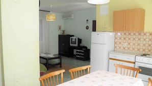 A compact kitchen with a refrigerator, stove, and wooden cabinets. There is a dining table with chairs and a television in the background. - Holiday apartment with air conditioning (Baška)
