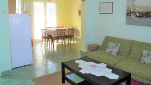 A living room with a green sofa, a coffee table with a lace doily, and a dining area with a table and chairs. - Holiday apartment with air conditioning (Baška)