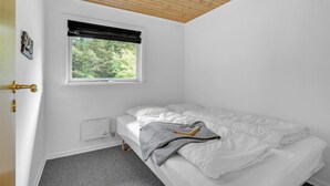 Une chambre avec un lit simple, une fenêtre donnant sur des arbres, un radiateur et une porte avec une poignée en laiton.