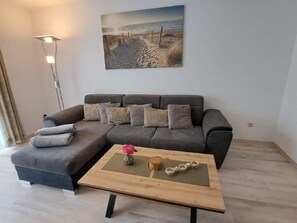 A modern living room with a grey sectional sofa, a wooden coffee table with decorative items, and a painting of a beach scene on the wall.