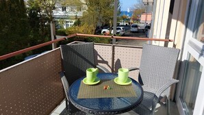 Un balcón con una mesa redonda, dos sillas y dos tazas verdes.