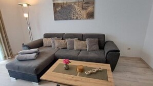 Una sala de estar moderna con un sofá seccional gris, una mesa de centro de madera con objetos decorativos y un cuadro de una escena de playa en la pared.