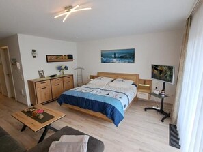 A bedroom with a bed, bedside table, TV, and a desk.