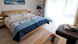 Una habitación de hotel con una cama, una mesita con un florero, un sofá, un televisor y un cuadro en la pared.