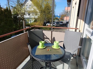 A balcony with a round table, two chairs, and two green cups.