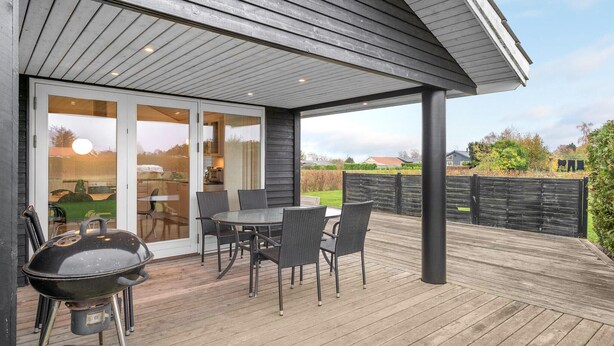 Un patio esterno coperto con tavolo e sedie, un barbecue e vista sul giardino.