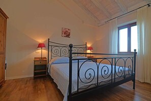 Een slaapkamer met een metalen bedframe, twee nachtkastjes met lampen, een houten garderobe en een raam met gordijnen.
