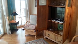 Un accogliente soggiorno con una poltrona in vimini, un mobiletto in legno con un televisore e un tavolino con una lampada.
