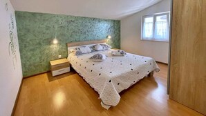 Un dormitorio con cama, mesita de noche, cómoda, ventana y pared verde.