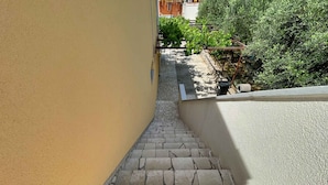 Una escalera exterior estrecha que lleva a un jardín en la azotea, con un sendero de piedra y una pared amarilla.